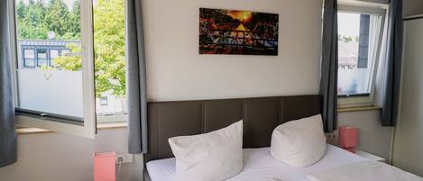 A hotel room with a bed, a nightstand, a painting, and a window with curtains.