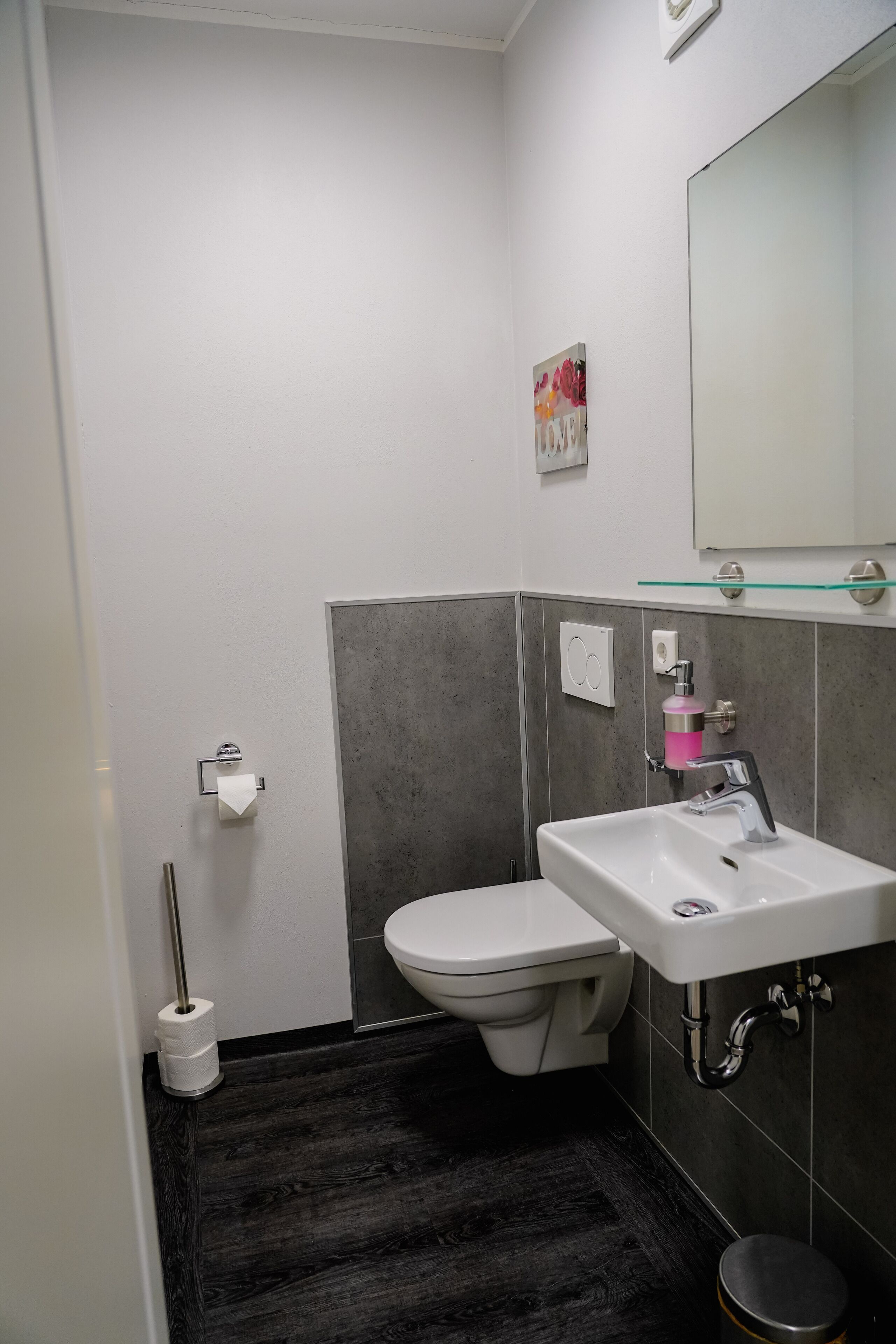 A modern bathroom with a toilet, sink, and a glass shelf above the sink.