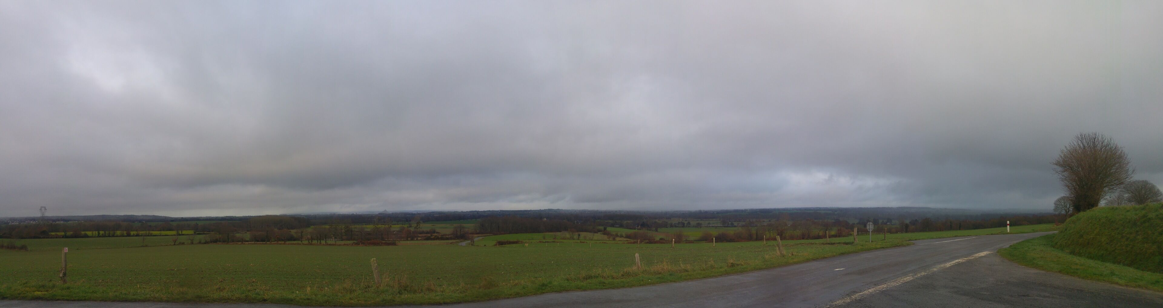 A rural road curving through fields with a cloudy sky.