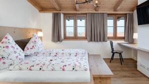 Une chambre avec un plafond en bois, un lit recouvert d’une literie à motifs floraux, un bureau et une chaise.