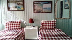 A room with two beds, each with a checkered bedspread, a nightstand with a lamp, and two framed pictures on the wall. - "We Make Your Stay In The Bahamas Both Comfortable and Affordable" (Governors Harbour)