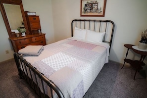 A bedroom with a bed, dresser, mirror, and a small table with a plant.