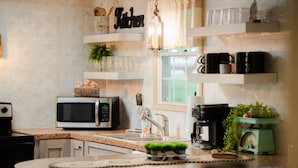 A kitchen with a microwave, coffee maker, and shelves with kitchenware.