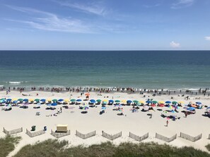 Une plage parsemée de nombreux parasols colorés et de chaises de plage, une étendue de sable et une vue dégagée sur l’océan.