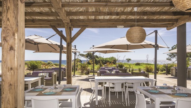 An outdoor dining area with white tables and chairs, large umbrellas, and a view of the sea. - Résidence Odalys Acqua Bella (Poggio-Mezzana)