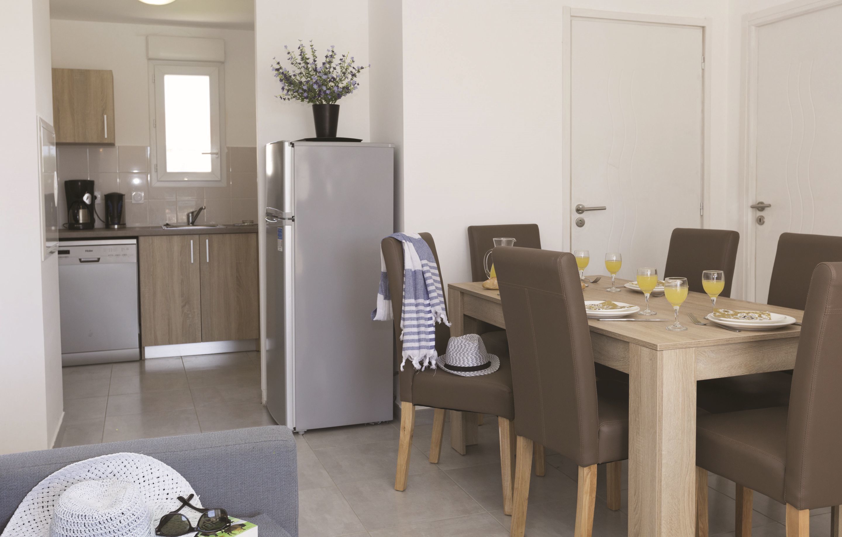 A modern kitchen with wooden cabinets, a refrigerator, and a dining area with a table set for two.