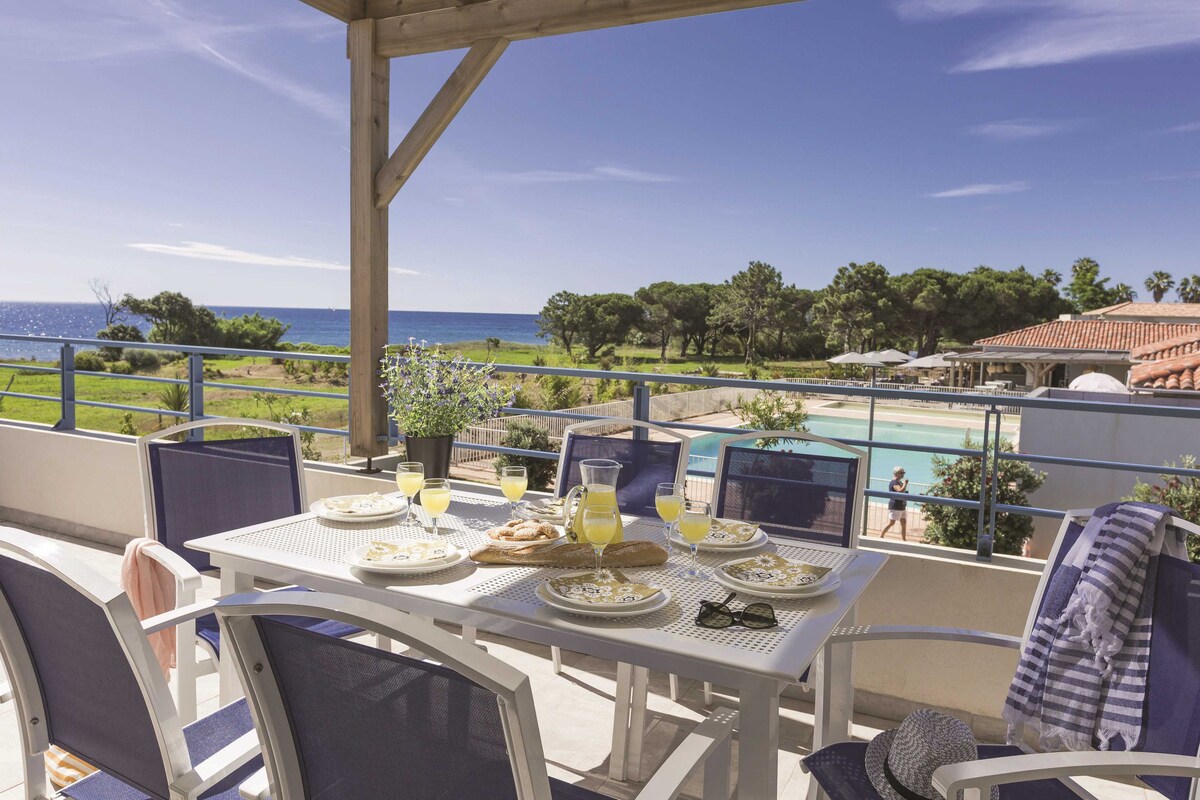 Una terraza con mesa lista para el desayuno, con vistas a una piscina y al mar.