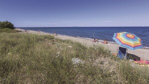 A beach with a colorful umbrella, a chair, and a person sunbathing. - Résidence Odalys Acqua Bella (Poggio-Mezzana)