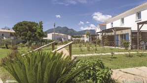 A residential area with houses, a grassy courtyard, and mountains in the background. - Résidence Odalys Acqua Bella (Poggio-Mezzana)