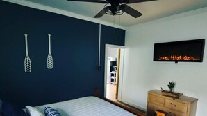 Een slaapkamer met een bed, een houten dressoir, een plafondventilator en een haard aan de muur.
