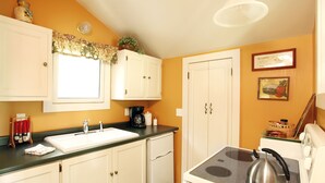 A compact kitchen with white cabinets, a sink, a stove, and a window with a floral curtain. - Romantic, 1 bedroom cottage walking distance to downtown, pet friendly, private. (Eureka Springs)