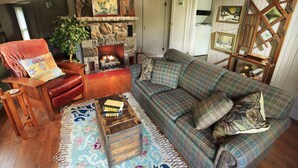 A cozy living room with a fireplace, a sofa, a chair, and a wooden coffee table. - Romantic, 1 bedroom cottage walking distance to downtown, pet friendly, private. (Eureka Springs)