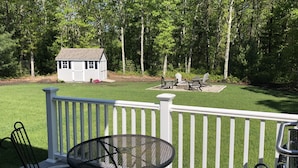 A deck with a table and chairs, a small shed, and a fire pit area. - Immaculate Cape Cod Family Retreat- minutes from Ponds, Lakes, and Ocean! (Sandwich)