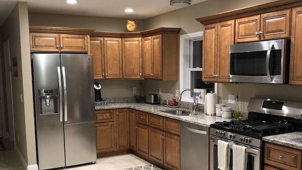 A modern kitchen with wooden cabinets, stainless steel appliances, and a tiled floor. - Immaculate Cape Cod Family Retreat- minutes from Ponds, Lakes, and Ocean! (Sandwich)