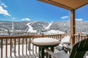 Eine Holzterrasse mit Tisch und Stühlen, mit Blick auf eine verschneite Berglandschaft und ein Skigebiet.