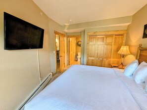 Ein Hotelzimmer mit einem großen Bett, einem flachbildfernseher an der Wand, Holztüren und einem Nachttisch mit einer Lampe.