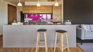 Een moderne keuken met houten kastjes, een centraal eiland met krukken, hanglampen en uitzicht op de woonkamer.