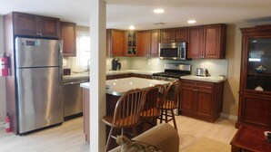 A modern kitchen with stainless steel appliances, wooden cabinets, and a central island with chairs.