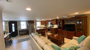 A spacious living area with a sofa set, a dining table with chairs, a kitchen area with modern appliances, and a television in a cabinet.