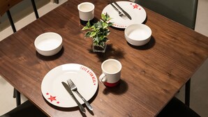 Una mesa de comedor dispuesta con platos, cubiertos y una pequeña planta en maceta.