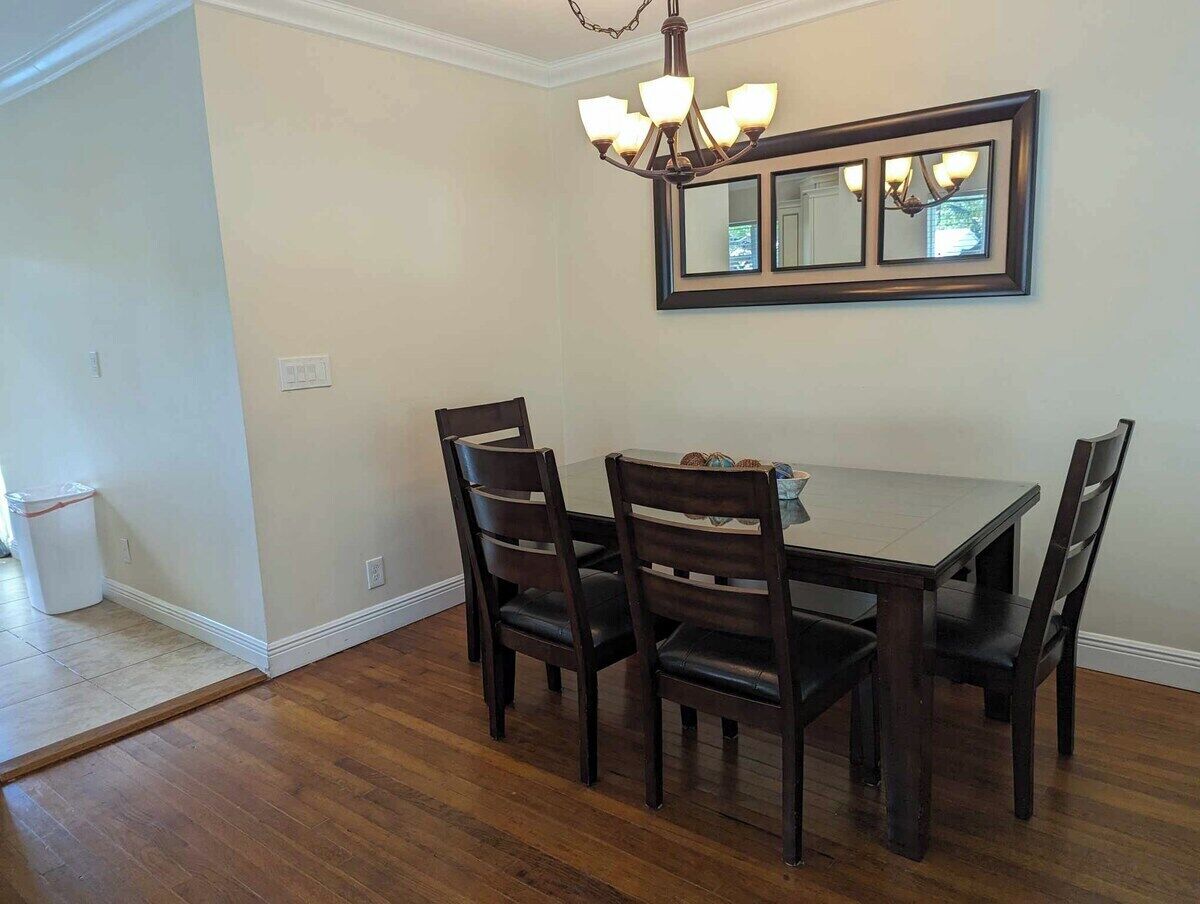 A dining area with a dark wooden table and chairs, a chandelier, and a wall-mounted mirror.