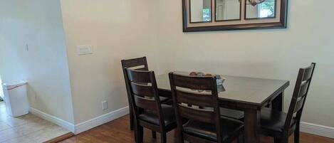 A dining area with a dark wooden table and chairs, a chandelier, and a wall-mounted mirror.