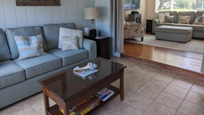 Un salon avec un canapé gris, une table basse, une lampe et une grande fenêtre avec des stores.
