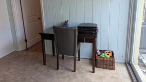 Een kamer met een stoel, een klein tafeltje, een printer en een mand met speelgoed.