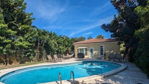 Une piscine dotée d’une terrasse carrelée, entourée de chaises longues et d’un espace barbecue couvert.