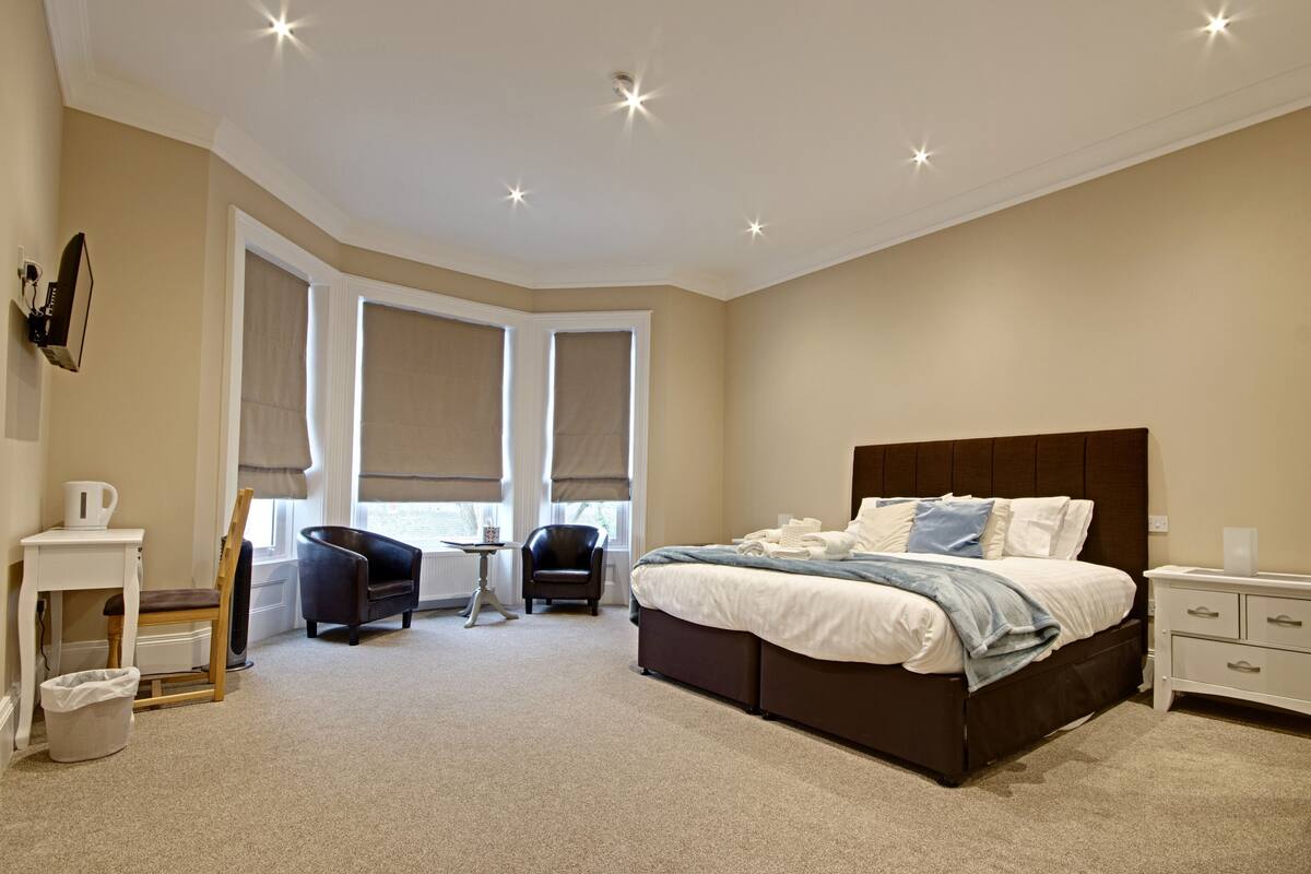 A modern bedroom with a large bed, two chairs, a small table, and a nightstand.