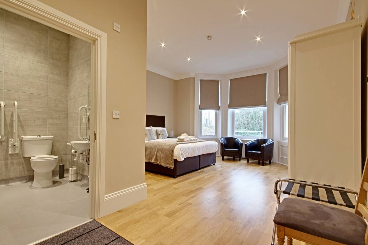 A bedroom with a large bed, a bedside table, a chair, and a window with blinds.