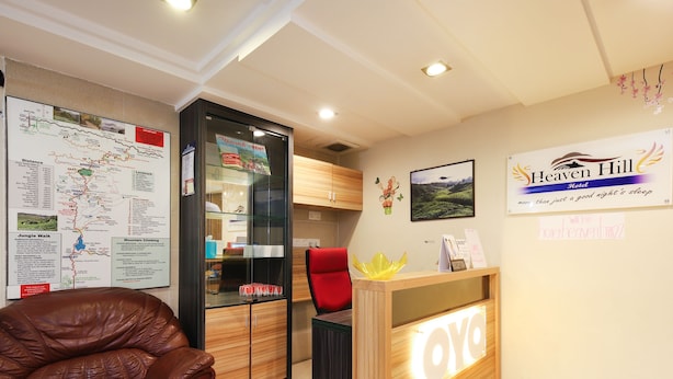 A hotel reception desk with a wooden counter and a sign that reads "Heaven Hill Hotel." There is a leather chair to the left and a map on the wall to the left of the reception desk. - OYO 1153 Heaven Hill Hotel 1 (Tanah Rata)