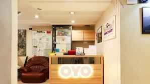 A reception desk with a wooden frame and a glowing 'OYO' sign, a brown leather sofa, a map on the wall, and a refrigerator with a 'Welcome' sign. - OYO 1153 Heaven Hill Hotel 1 (Tanah Rata)