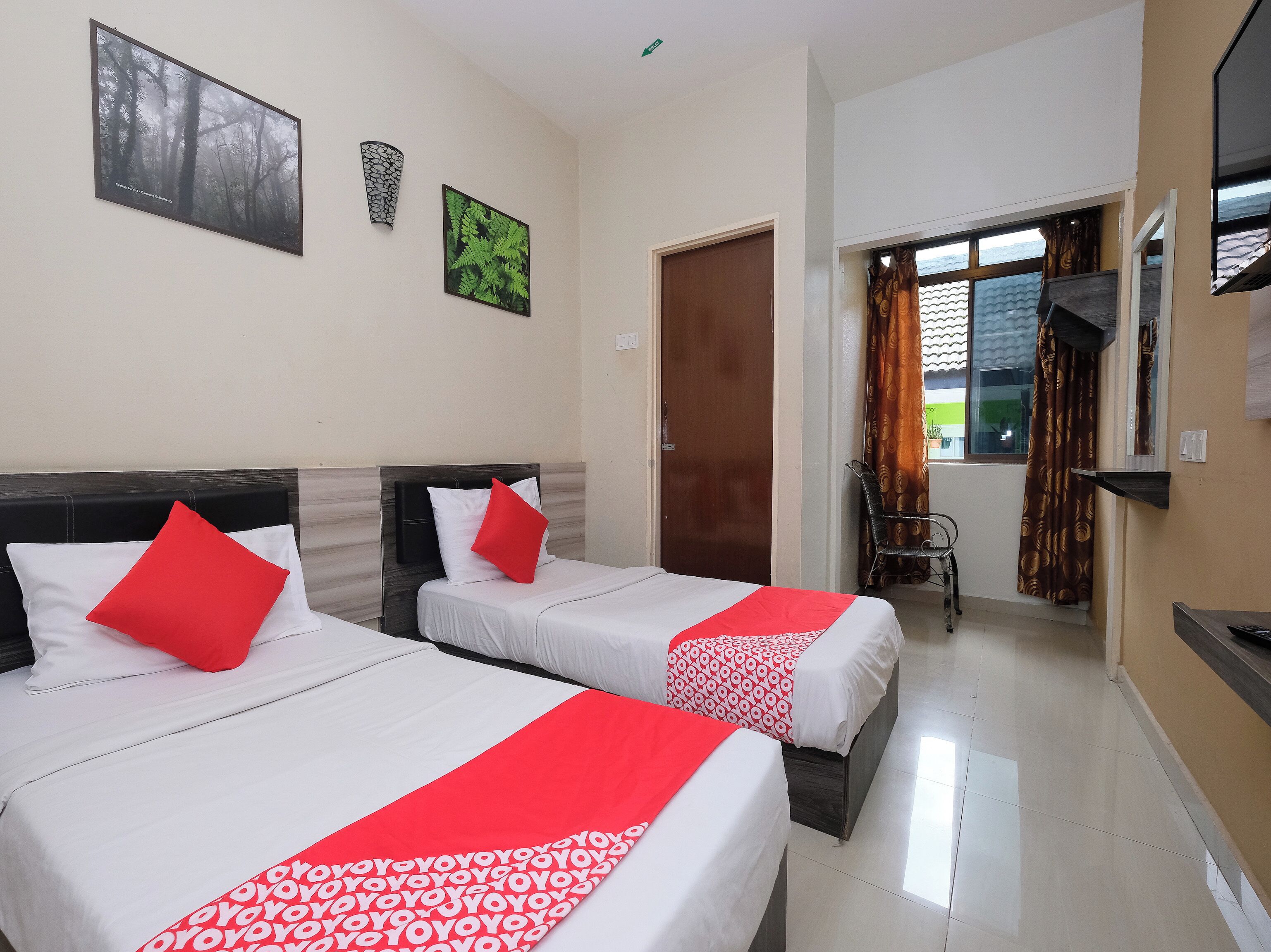 Two single beds with red and white bedding, a wooden door, a small table, and a window with curtains.