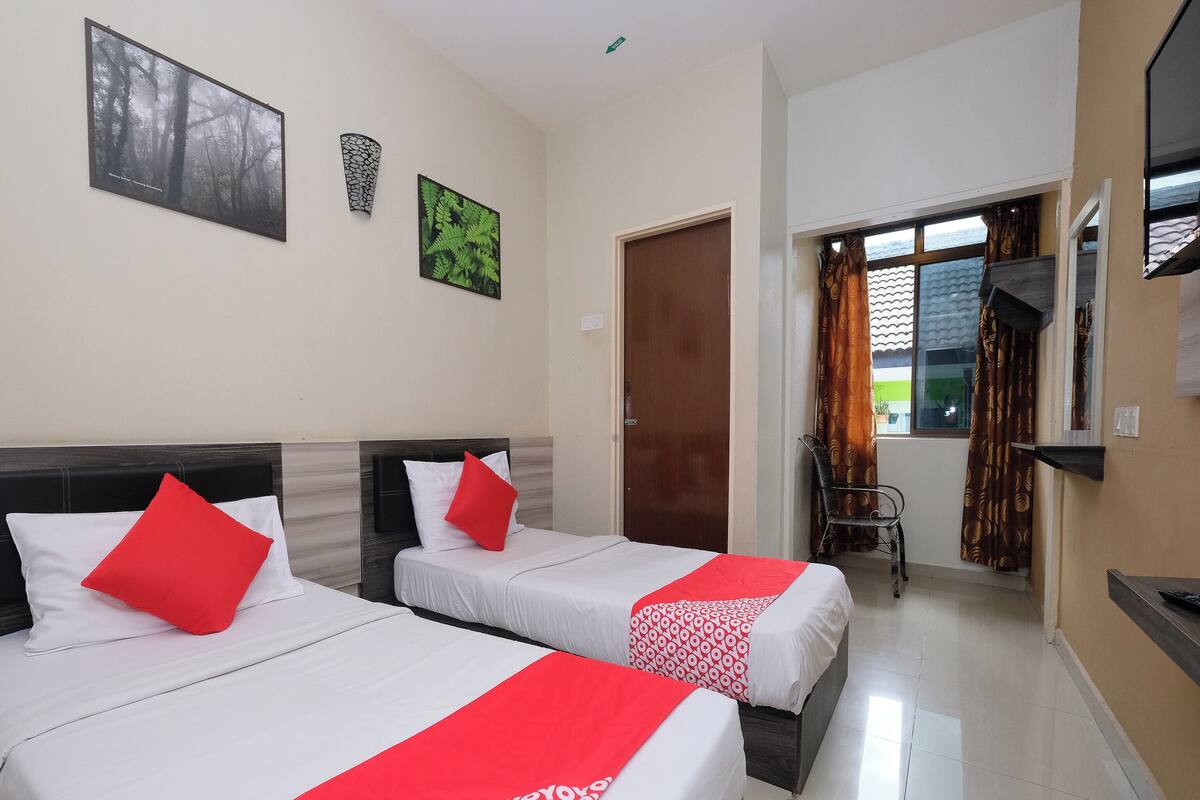 Two single beds with red and white bedding, a wooden door, a small table, and a window with curtains.