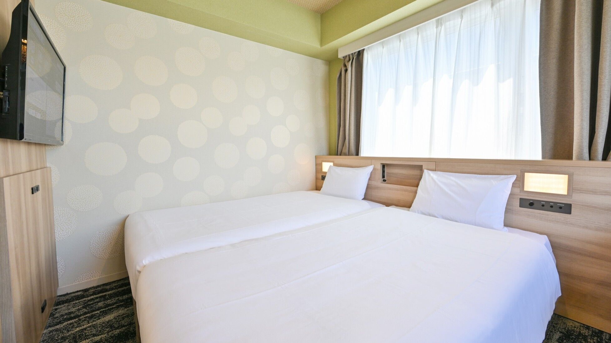 A hotel room with a large bed, a TV, and a window with curtains.