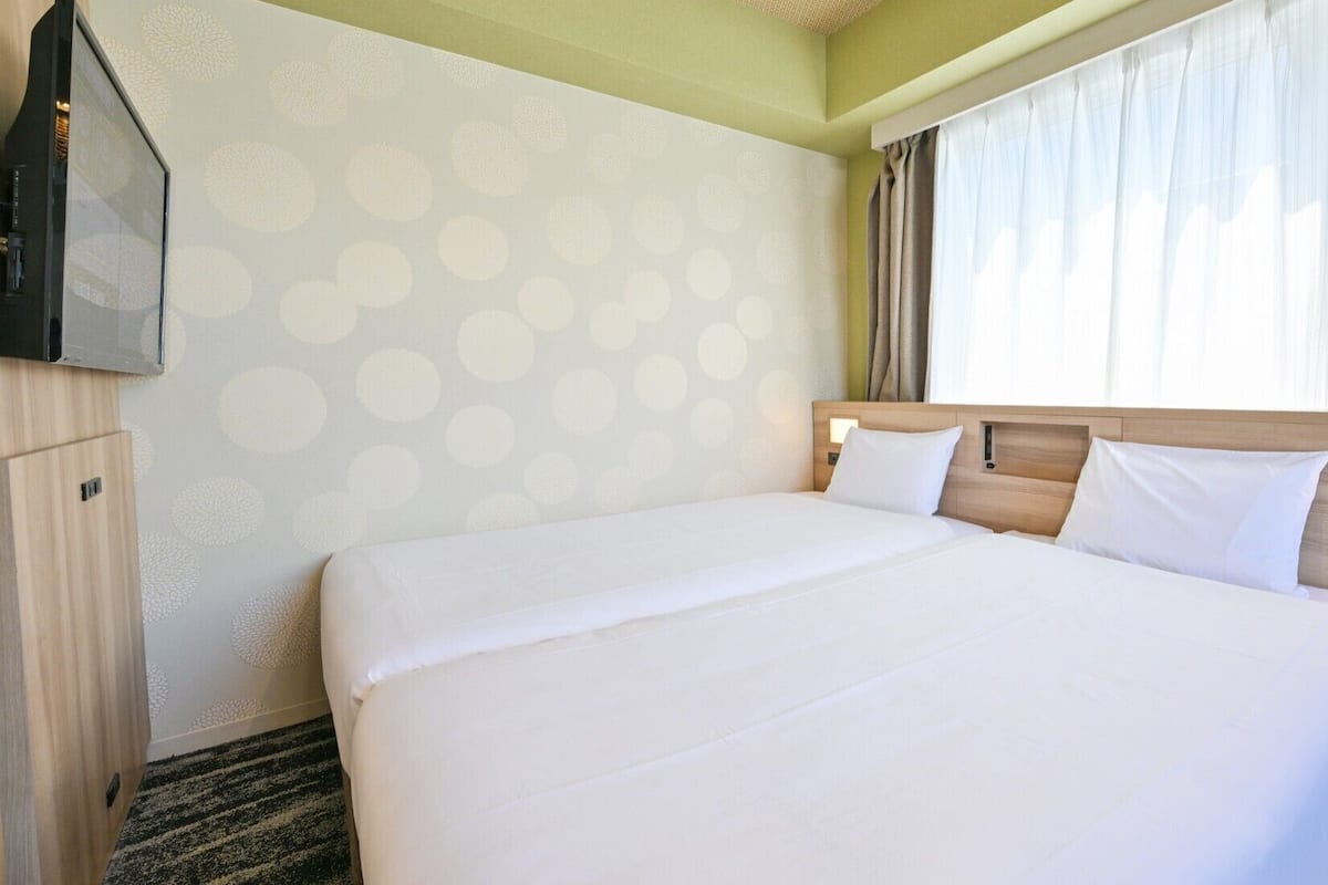 A hotel room with a large bed, a TV, and a window with curtains.