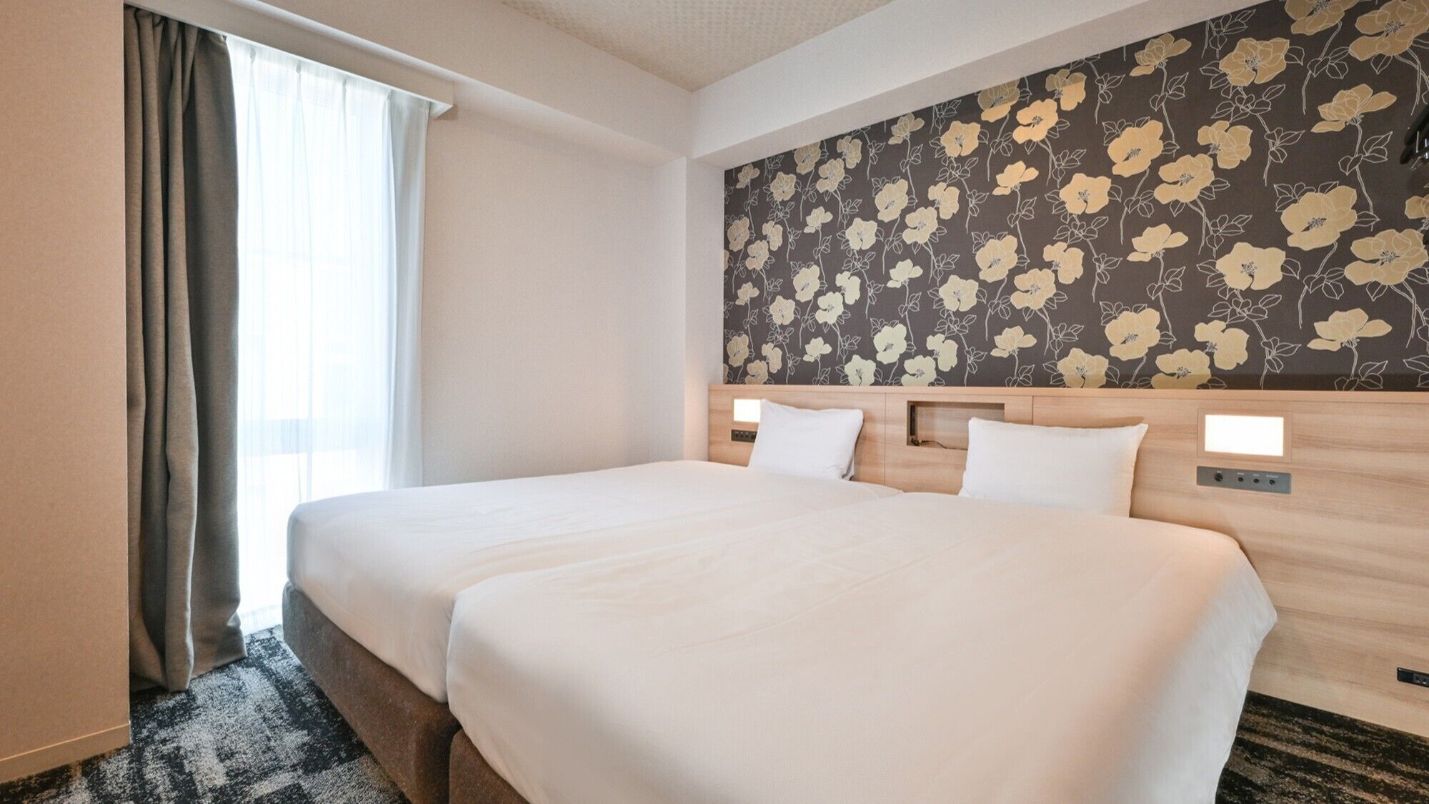 A hotel room with a large bed, a wooden headboard, a floral wallpaper, and a window with curtains.