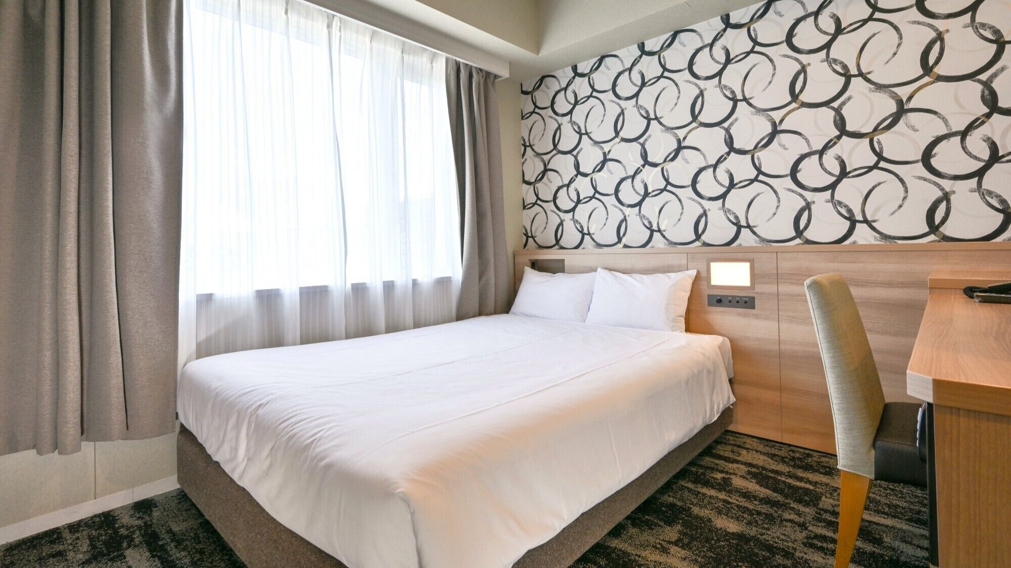 A hotel room with a large bed, a desk, and a patterned wall.