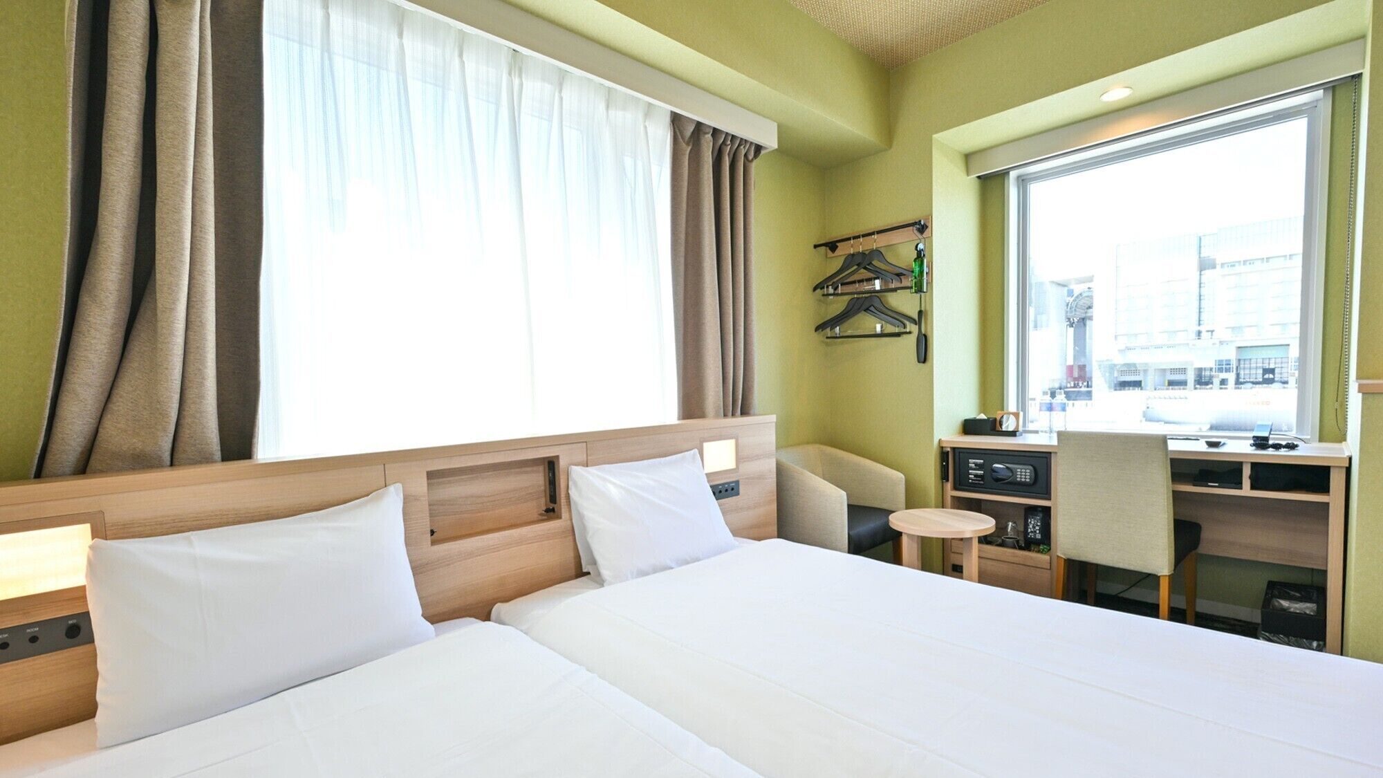 A hotel room with a bed, a desk, a chair, a small table, and a window with curtains.