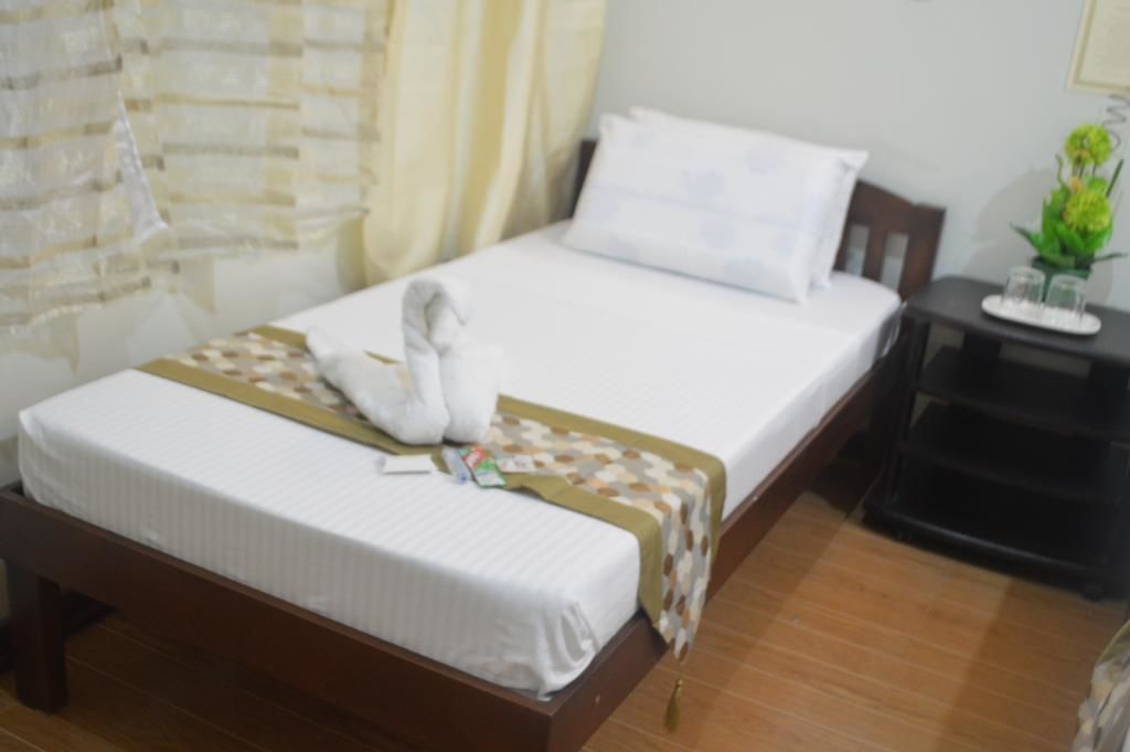 A neatly made bed with a white comforter and a brown blanket, a small bedside table with a tray, and a potted plant on the nightstand.