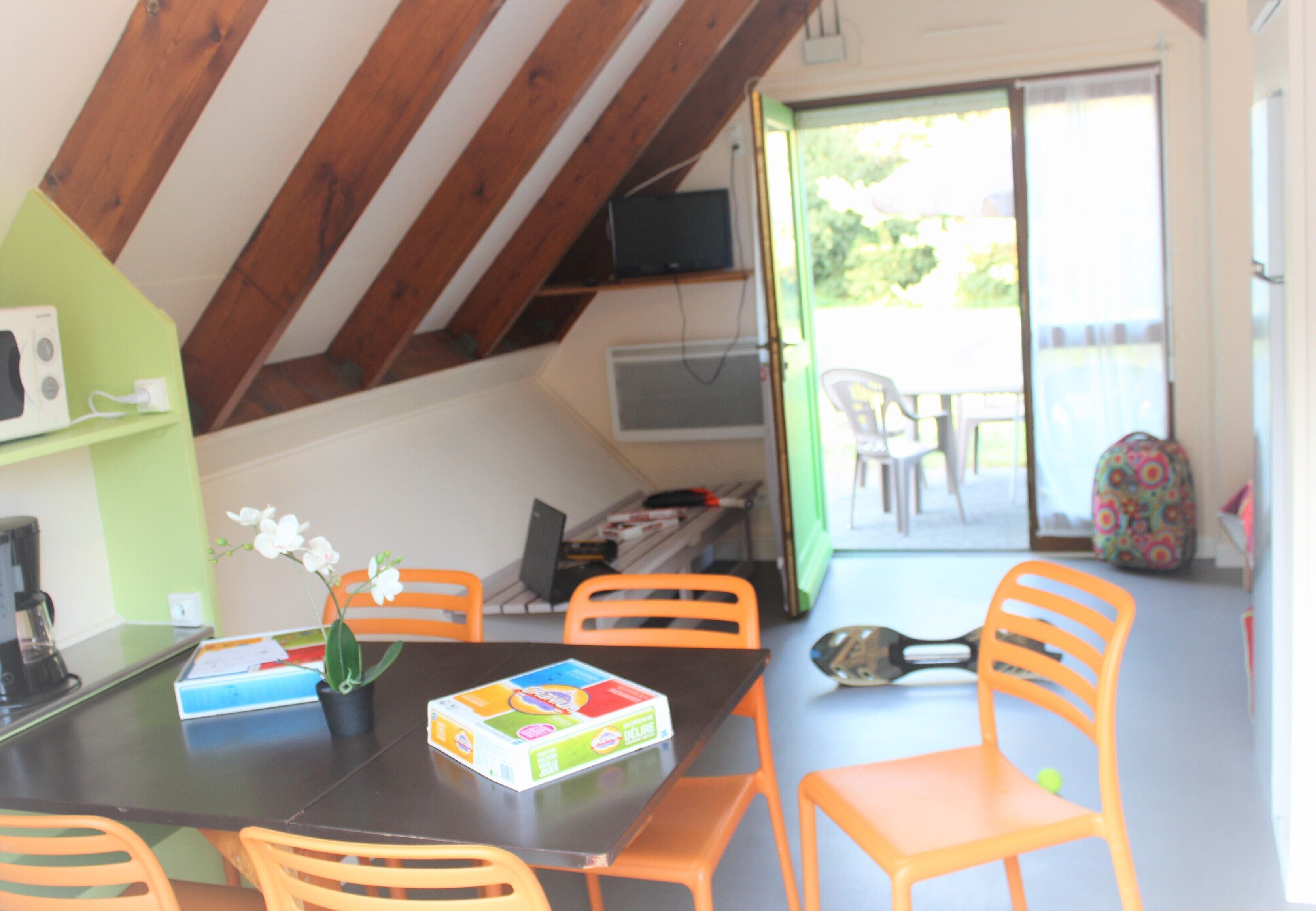 A dining area with a table set for four, surrounded by orange chairs. A potted plant and a children's toy box are on the table.