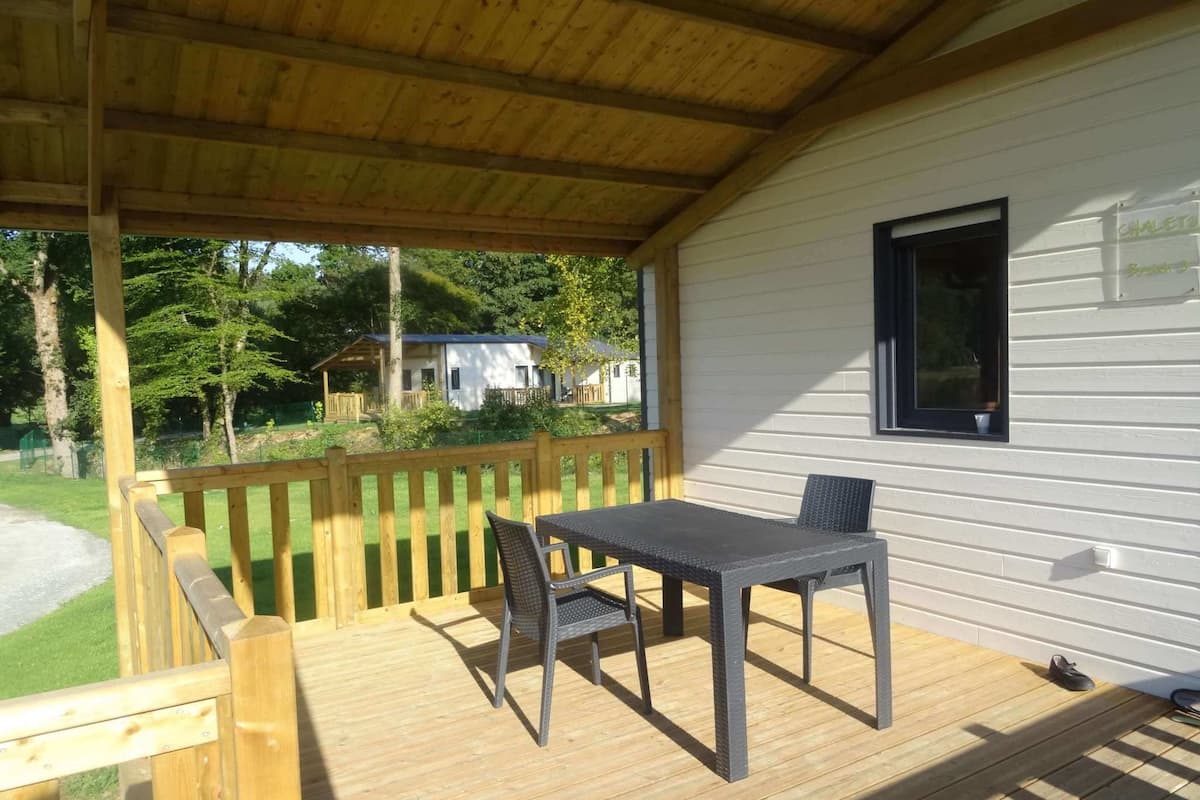 A covered outdoor area with a wooden deck, a table, and two chairs.
