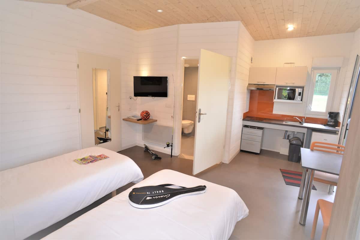A compact hotel room with two beds, a small kitchenette, a TV, and a bathroom.
