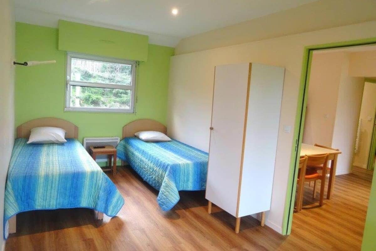 A room with two single beds, a window, a wooden table, and a wardrobe.