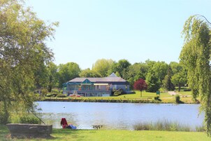 Un edificio frente a un lago con un muelle, rodeado de exuberante follaje y árboles.