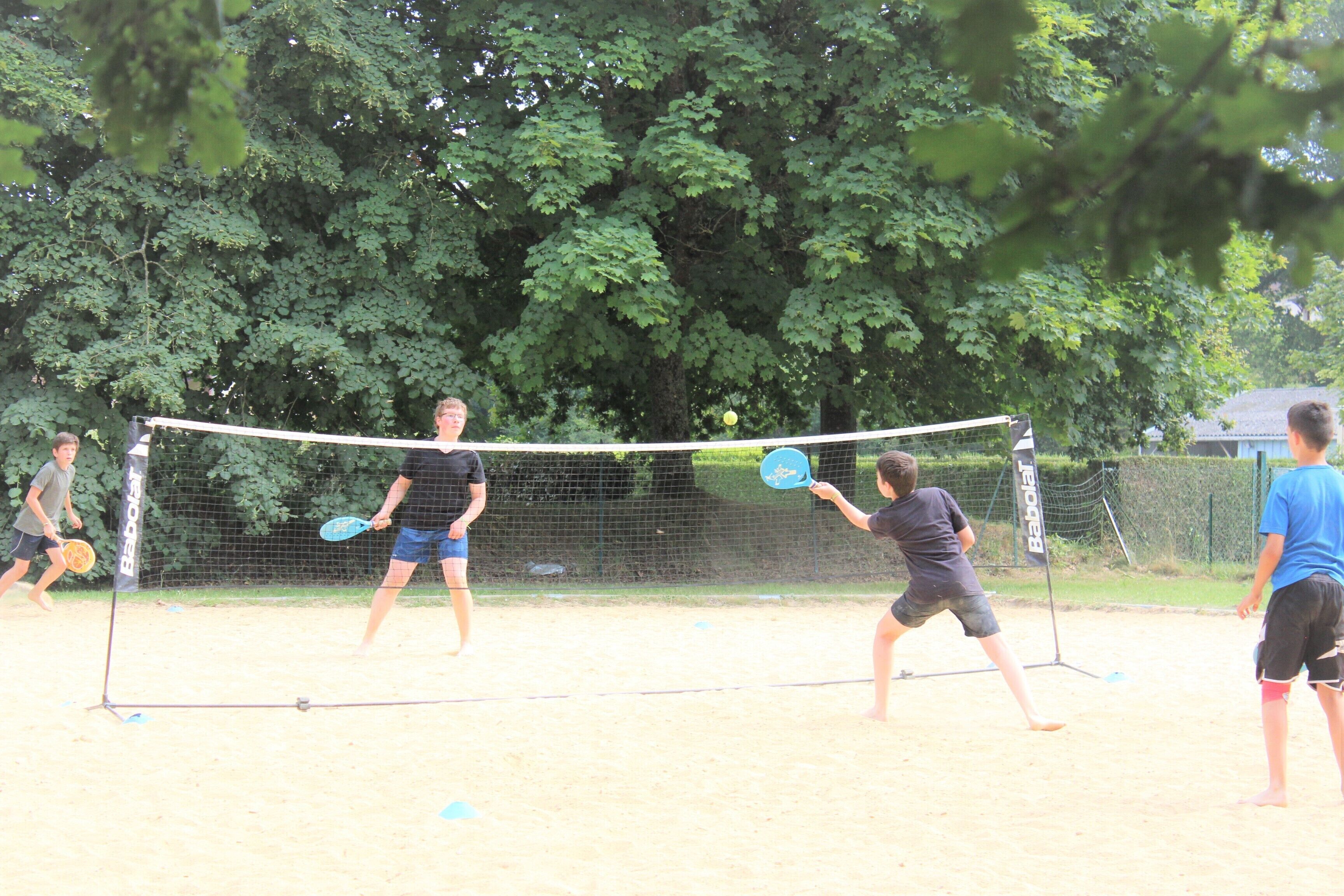 A sandy outdoor volleyball court with a net, surrounded by trees.