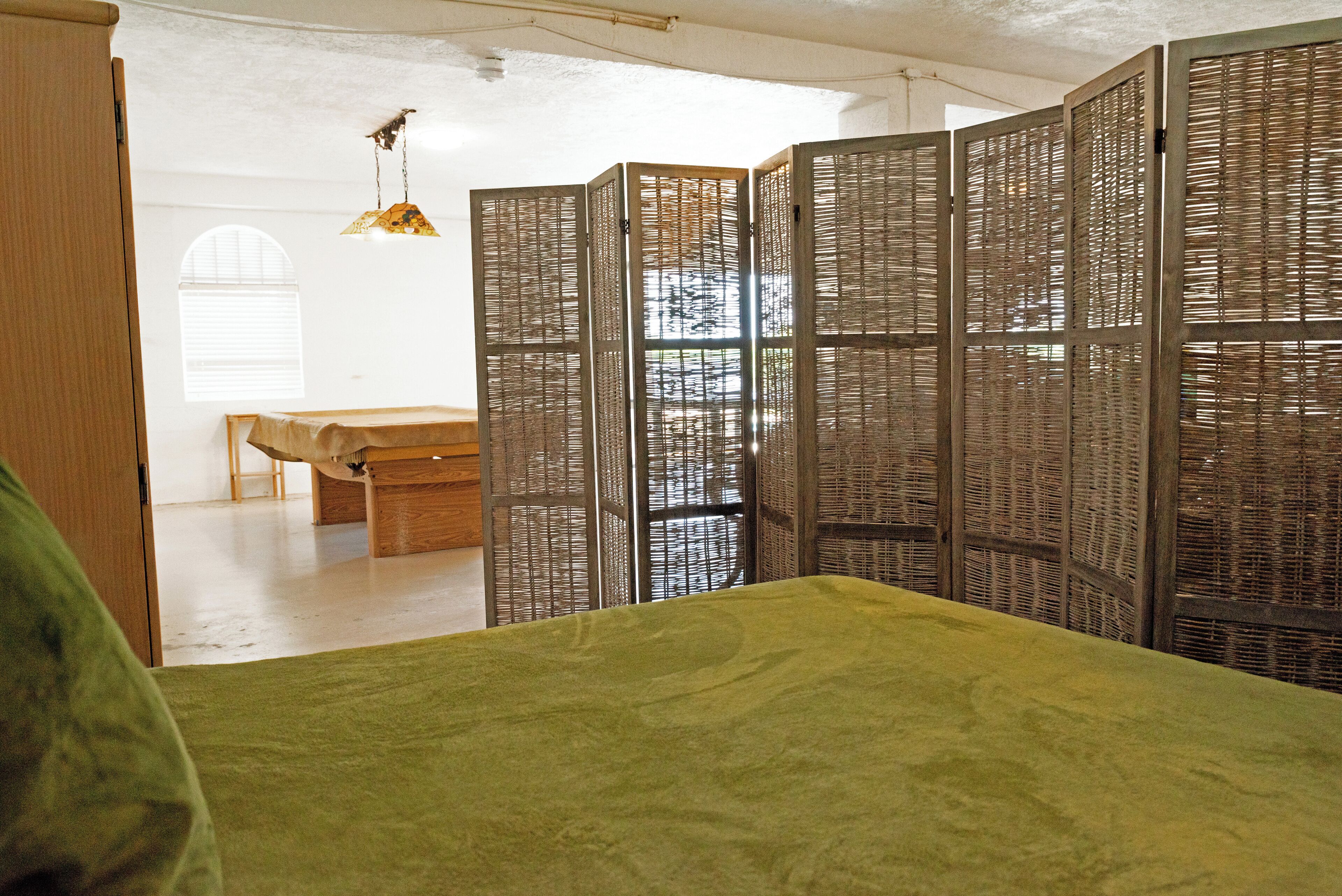 A room with a green bed, a wooden bench, and a room divider with vertical slats.