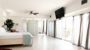 A spacious bedroom with a large bed, a ceiling fan, a TV mounted on the wall, and a sliding glass door leading to a balcony. - Seaside Sanctuary 5 bed, 5 bath pool home (Tavernier)