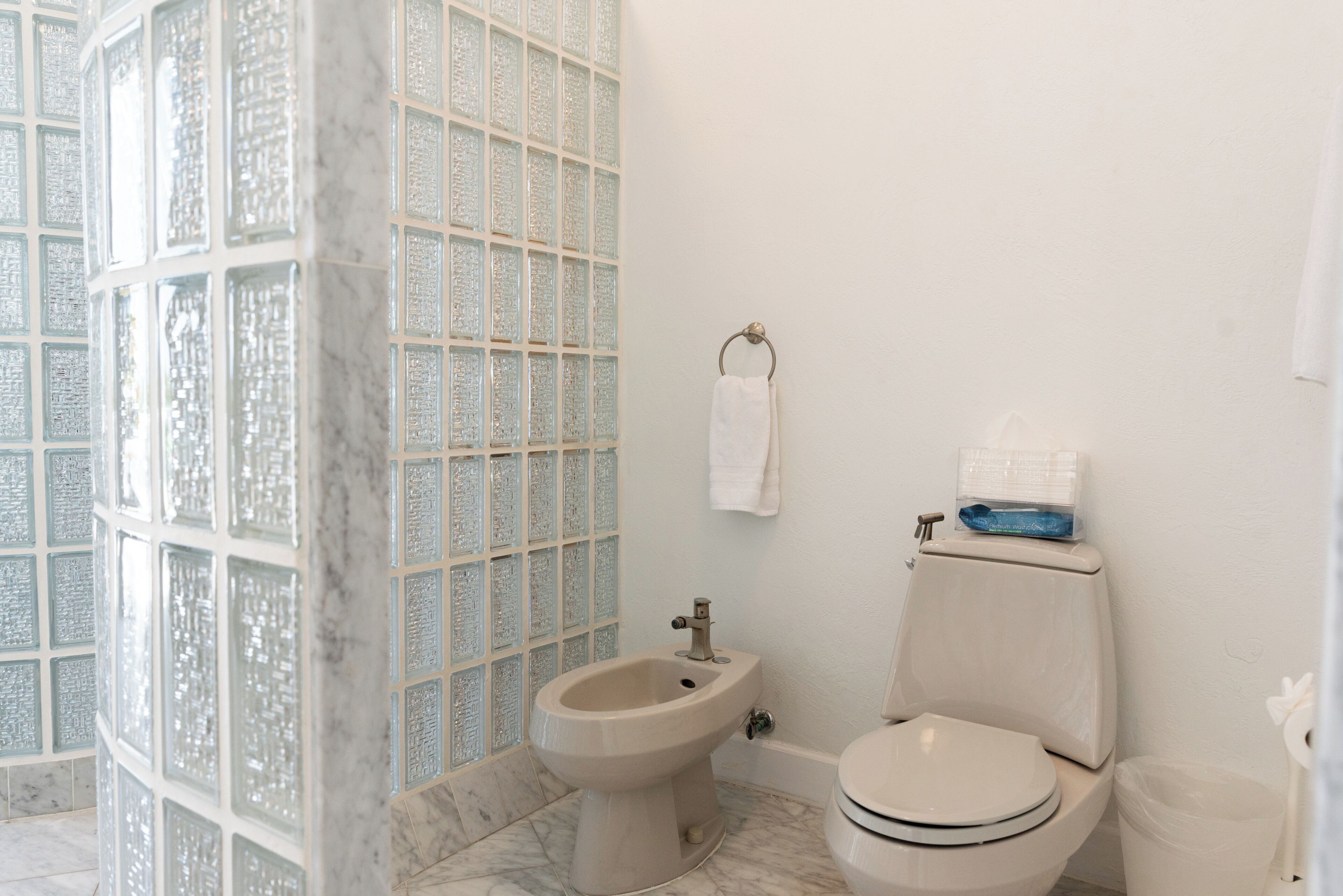 A bathroom with a marble floor, a bidet, a toilet, and a glass shower enclosure.